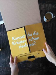 Photo of a half-open, sunny yellow SONNENTOR shipping carton signed by the person who packed the carton. | © SONNENTOR