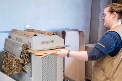 The photo shows a SONNENTOR employee shredding cardboard. | © SONNENTOR