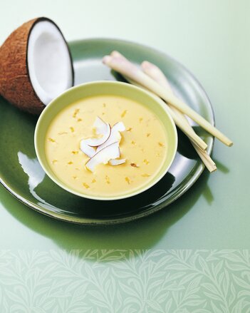 Auf dem Foto ist ein Teller mit Kokos-Curry-Suppe zu sehen. Drin sind kleine Kokosstückchen zu sehen. Dahinter sieht man eine halbe Kokosnuss. | © SONNENTOR