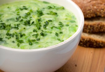 Auf dem Foto sieht man eine Schüssel mit Zucchinisuppe. Darüber ist Schnittlauch gestreut. Im Hintergrund sieht man Brot. | © SONNENTOR