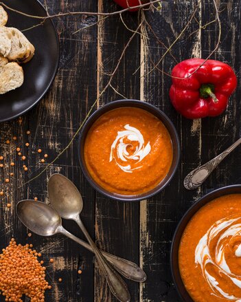 Auf dem Foto ist ein Schälchen mit Paprikaschaumsuppe zu sehen. Daneben liegen Paprika, Linsen und zwei Löffel. | © SONNENTOR