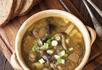 Auf dem Foto ist die Bramboracka Znaimer Kartoffelsuppe mit Pilzen auf einem Holzbrett zu sehen. Daneben liegen mehrere Scheiben Brot. | © SONNENTOR