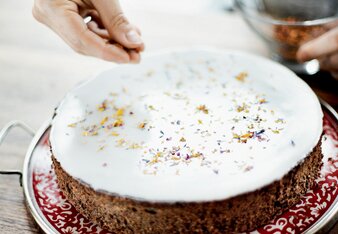 Auf dem Foto ist eine Flower Power Mohntorte zu sehen. Man sieht wie jemand die Gewürzblütenmischung auf die Torte streut. | © SONNENTOR