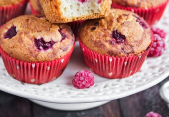 Auf dem Foto sind mehrere Himbeermuffins zu sehen. Daneben sind frische Himbeeren und Staubzucker zu sehen. | © SONNENTOR