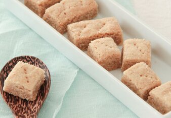 Auf einem weißen Servicetablett sind die hellen Chai Shortbread zu sehen. Daneben liegt ein Holzlöffel mit einem Chai Shortbread darauf. | © SONNENTOR