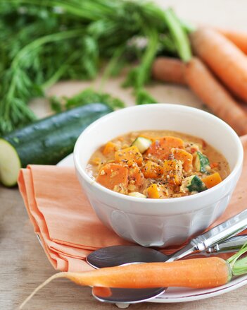 Auf dem Foto ist eine Schale mit Linsencurry mit Süßkartoffeln zu sehen. Daneben sieht man Karotten und Zucchini. | © SONNENTOR