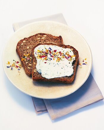 Auf dem Foto ist Brot mit dem Gute Laune Kräutertopfen zu sehen. Darüber gestreut ist das bunte Gute Laune Gewürz. | © SONNENTOR