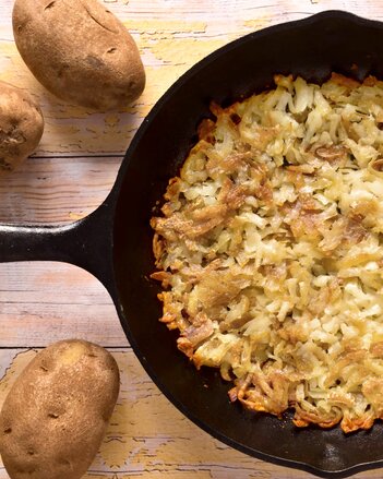 Auf dem Foto ist eine Pfanne mit Kartoffelschmarrn zu sehen. Daneben liegen ganze Kartoffeln. | © SONNENTOR