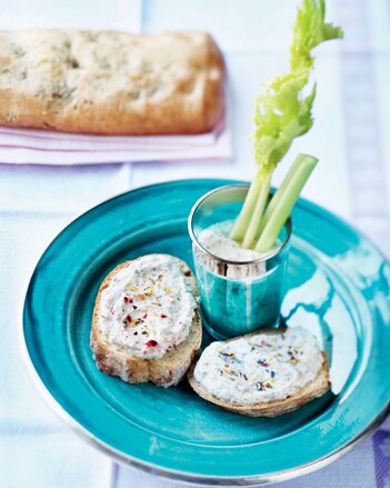 Auf dem Foto ist ein blauer Teller mit zwei Scheiben Brot und Schutzengel Joghurt Aufstrich zu sehen.  Daneben ist der Dip mit Sellerie zu sehen. | © SONNENTOR