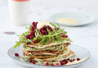 Auf dem Foto ist ein Turm von Rucola-Pancakes zu sehen. Darauf sind frischer Rucola und Granatapfelkerne zu sehen. | © SONNENTOR