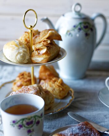 Auf dem Foto ist eine Etagere mit Apfelstrudel Fingerfood zu sehen. Davor steht eine Tasse Tee und im Hintergrund ist eine Teekanne zu sehen. | © SONNENTOR