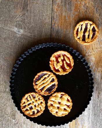 Foto von bunten Linzer-Tartalettes auf einem schwarzen Teller. | © SONNENTOR