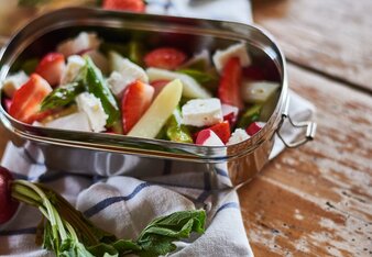 Foto von einer Dose mit buntem Spargelsalat und Feta. Rundherum sind Gemüse und Obst zu sehen. | © SONNENTOR