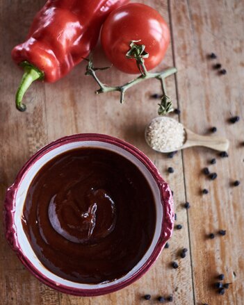 Auf dem Foto ist ein kleines Schüsselchen mit BBQ Sauce zu sehen. Daneben ist eine Paprika und eine Tomate zu sehen. | © SONNENTOR