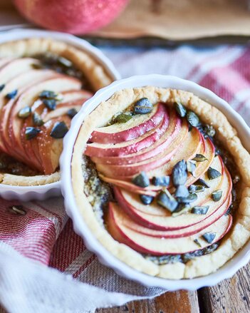 Auf dem Foto sind zwei Formen mit Apfeltartes zu sehen. Im Hintergrund ist ein Apfel zu sehen. | © SONNENTOR