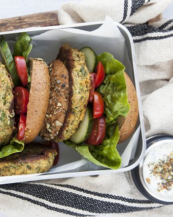 Auf dem Foto sieht man zwei Gemüse-Burger in einer Box liegen. Neben der Box steht ein kleines Schälchen mit Dip. | © SONNENTOR