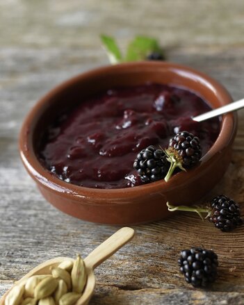 Auf dem Foto ist ein kleines Schälchen mit Brombeermarmelade zu sehen. Daneben liegen Kardamom Kapseln und frische Brombeeren. | © SONNENTOR