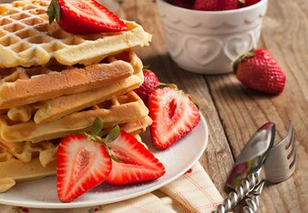 Auf dem Foto ist ein Teller voll mit Frühstückswaffeln und frischen Erdbeeren zu sehen. Dahinter steht ein Schälchen mit weiteren Erdbeeren. | © SONNENTOR