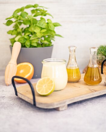 Auf dem Foto ist ein Tablett mit einem Glas Joghurtdressing zu sehen. Daneben sieht man eine halbe Limette und Orange, sowie zwei kleine Kännchen. | © SONNENTOR