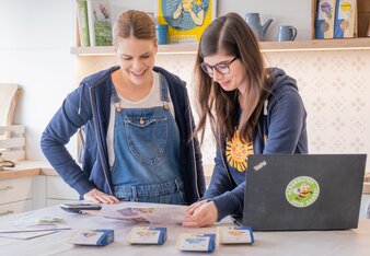 Das Bild zeigt zwei Mitarbeiterinnen, die gerade einen Folder anschauen, die Räuchermischungen liegen davor auf dem Tisch.  | © SONNENTOR