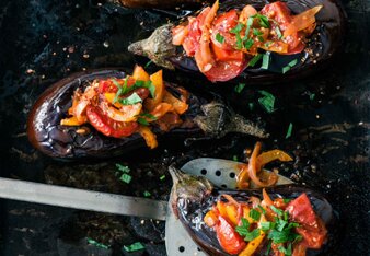 Foto von mehreren gefüllten Auberginen. Auf den Auberginen sind Tomaten, Paprika und Petersilie zu sehen. | © SONNENTOR