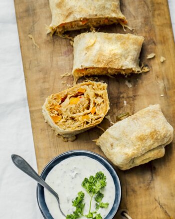 Auf dem Foto ist ein Holzbrett mit aufgeschnittenem Sauerkraut-Kimchi-Strudel zu sehen. Daneben steht eine Schüssel mit Dip. | © SONNENTOR