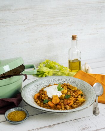 Auf dem Foto sieht man einen Teller mit Linsen-Curry-Eintopf. Der Eintopf ist mit einen Klacks Sauerrahm und Petersilie angerichtet. | © SONNENTOR