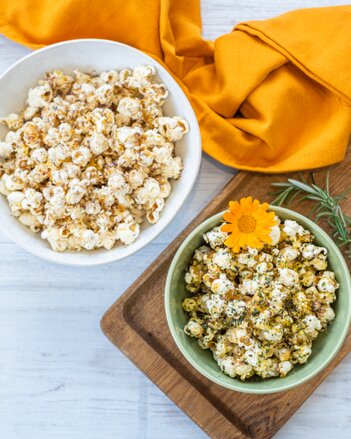 Auf dem Foto sind zwei Schüsseln mit Gewürzblüten Popcorn zu sehen. Darin ist auch eine orangene Blüte und ein Rosmarinzweig zu sehen. | © SONNENTOR