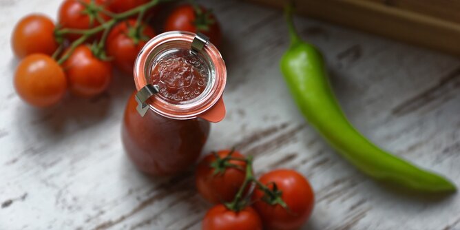 Auf dem Foto sieht man ein Glas mit selbstgemachtem Ketchup. Daneben sieht man frische Tomaten und einen grünen Paprika. | © SONNENTOR