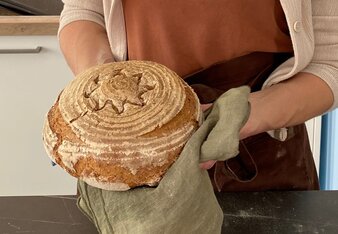 Auf dem Foto sieht man wie eine Frau einen Laib Brot mit einem Geschirrtuch hält.  | © SONNENTOR