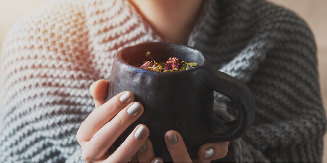 Auf dem Foto sieht man wie jemand eine Tasse mit verschiedenen Kräutern in den Händen hält. | © SONNENTOR